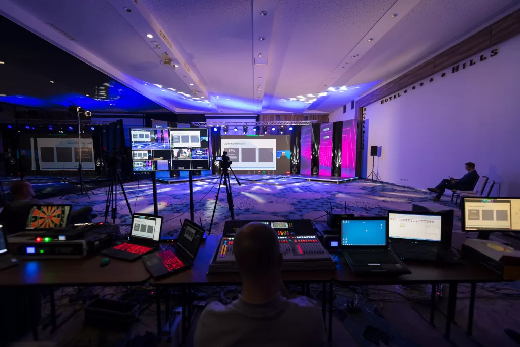 A professional live streaming setup in a large event space, showcasing multiple monitors, cameras, and technical equipment. The setup is prepared to capture and broadcast a high-quality live event, highlighting the intricate coordination and advanced technology involved in delivering seamless live streaming services.